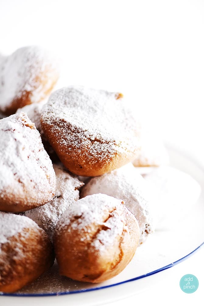 Beignets  on a plate dusted with powdered sugar - addapinch.com