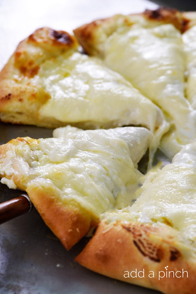 Golden brown crust edges on a cheesy Three Cheese White Pizza that's been sliced and is being lifted with server. 