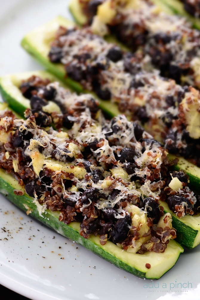 Rows of zucchini halves are stuffed with black beans, quinoa and shredded cheese on a platter.