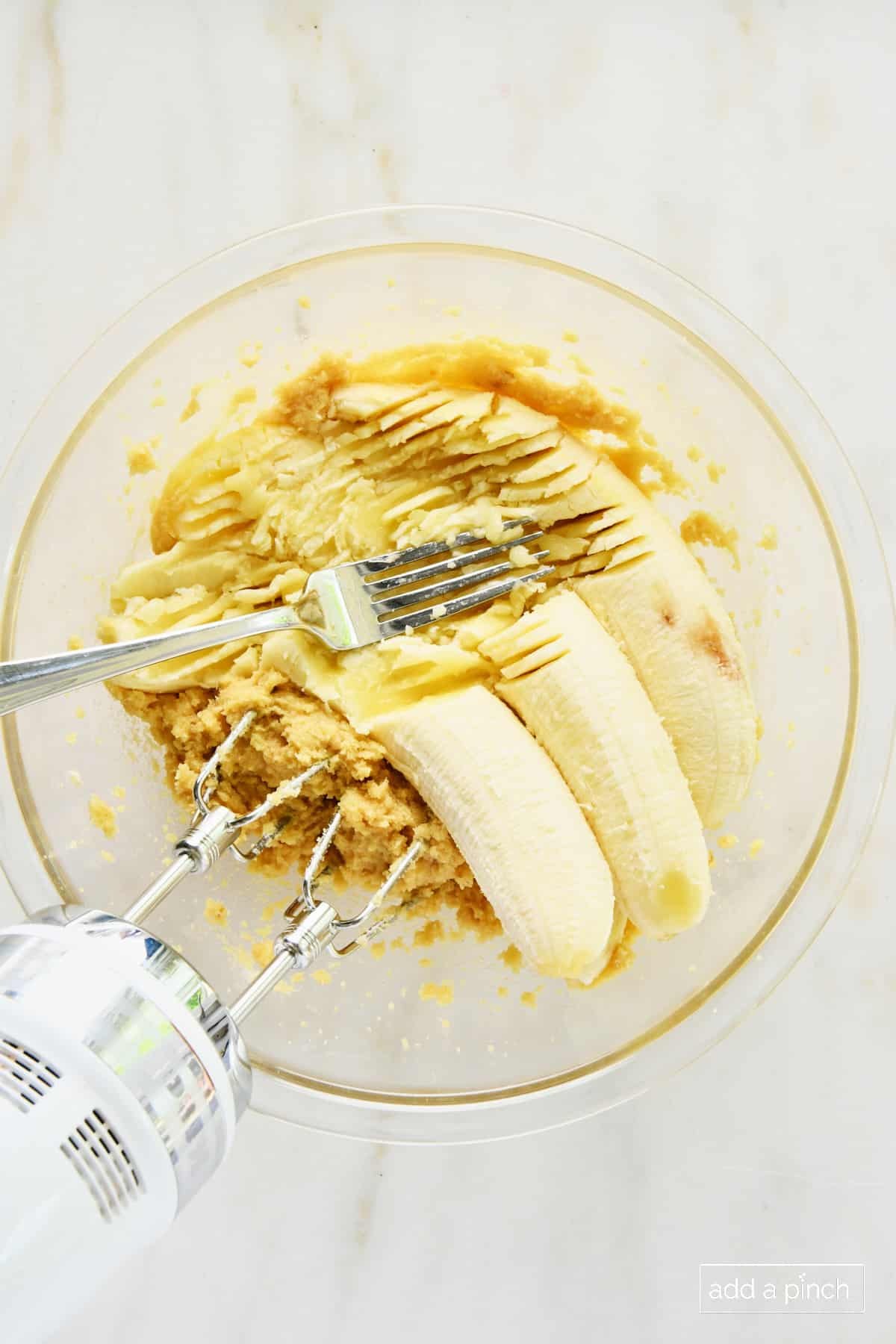 Bananas added to brown sugar and butter mashing with a fork in a glass bowl.
