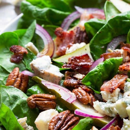Close photograph of spinach salad with pears, bacon, onion, and blue cheese.