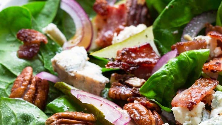 Close photograph of spinach salad with pears, bacon, onion, and blue cheese.