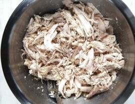 Shredded chicken in a mixing bowl on a marble counter.
