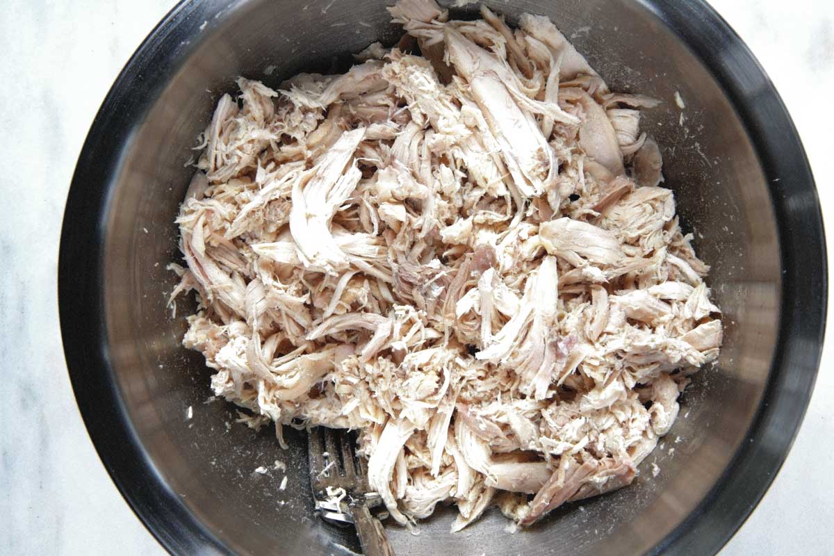 Shredded chicken in a mixing bowl on a marble counter. 