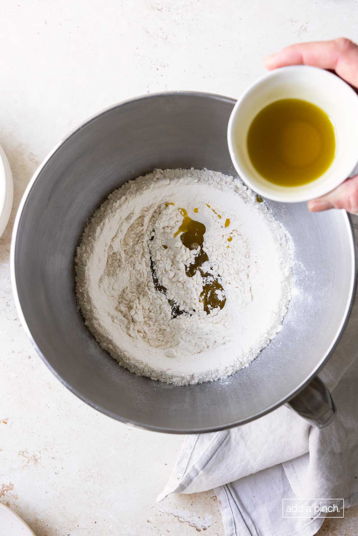 Olive oil being poured into a bowl with flour mixture to make pizza dough.