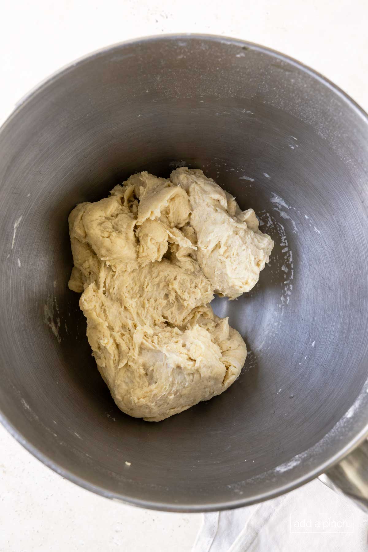 A ball of soft dough is beginning to form in the mixing bowl in order to make pizza dough.