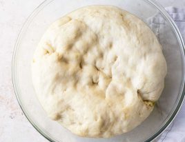 Pizza dough rising in a glass bowl