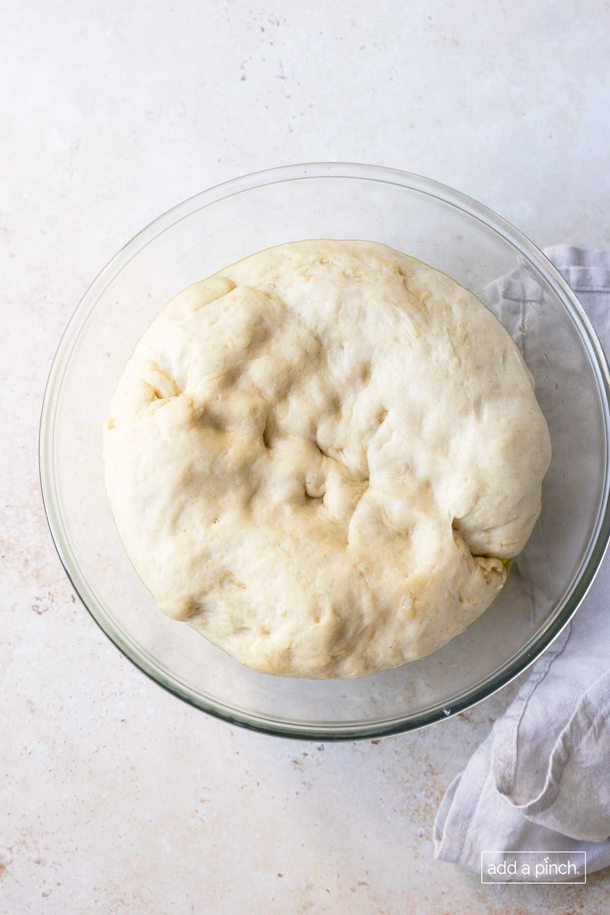 Pizza dough rising in a glass bowl.