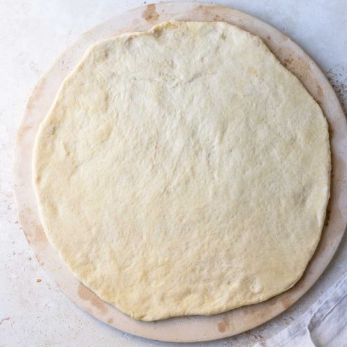 Pizza dough on a pizza stone ready for toppings.