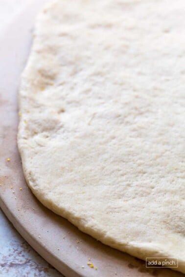 Photo of pizza dough on a wooden pizza peel ready to be topped with toppings and baked.