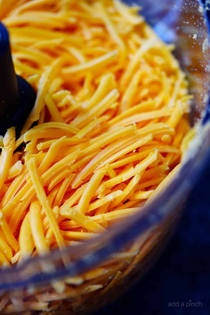 Shredded cheddar cheese in a glass bowl.