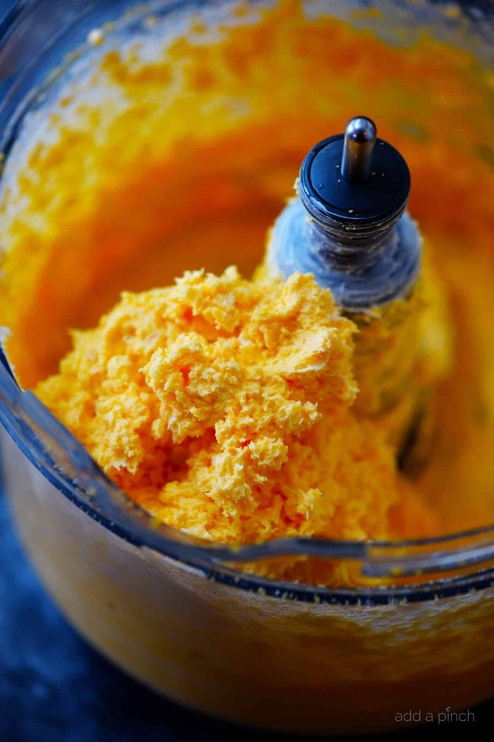 Cheese are combined in a food processor to cream them together to make pimento cheese.