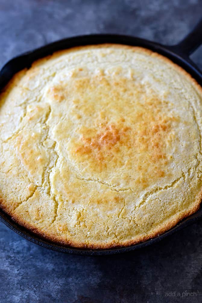 Golden brown cornbread with crisp edges in a cast iron skillet on a black granite counter // addapinch.com