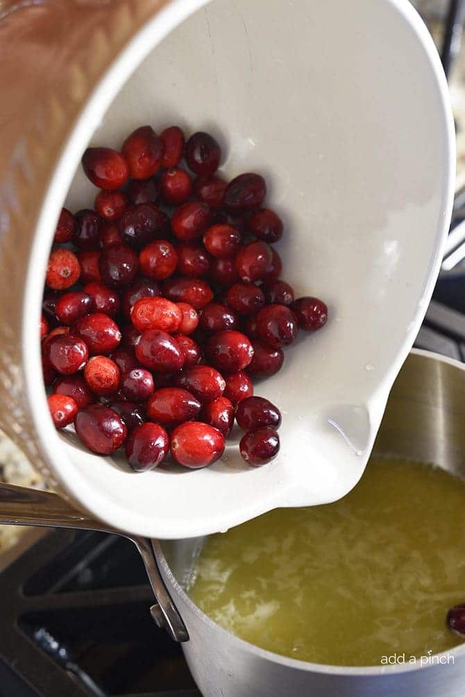 Adding fresh cranberries to saucepan of boiling orange juice, water and sugar. // addapinch.com