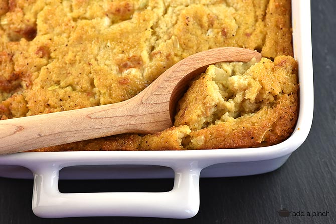 Moist Southern cornbread dressing with a wooden spoon in a white baking dish.