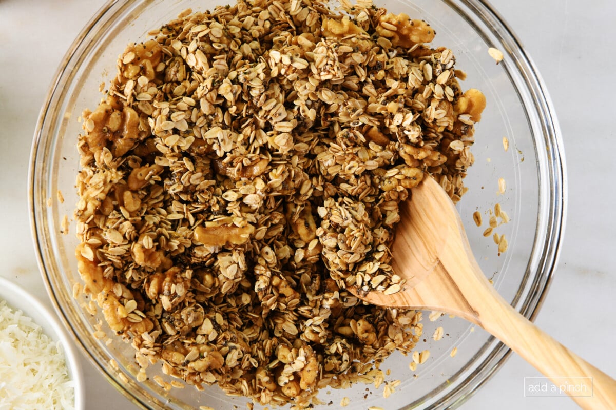 Granola mixture in a glass mixing bowl with a wooden spoon.