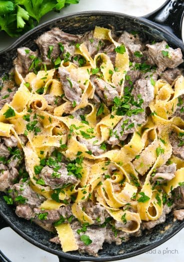 Photograph of beef stroganoff in a skillet with egg noodles and topped with parsley.