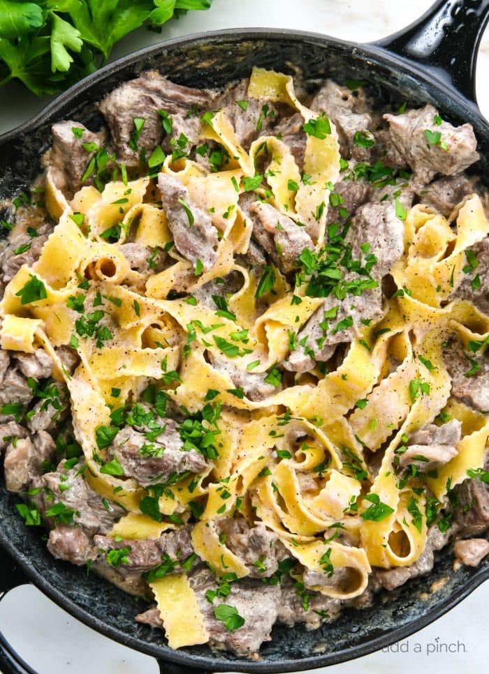 Photograph of beef stroganoff in a skillet with egg noodles and topped with parsley. 