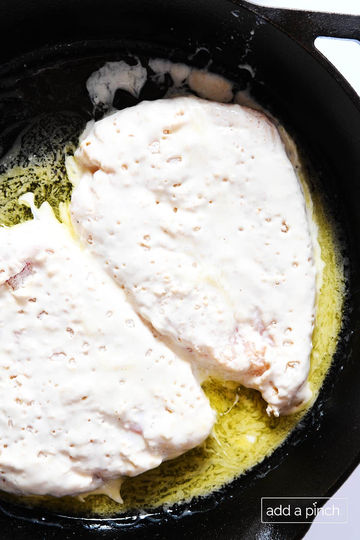 Breaded chicken breasts added to a cast iron skillet with butter to be cooked in the oven.