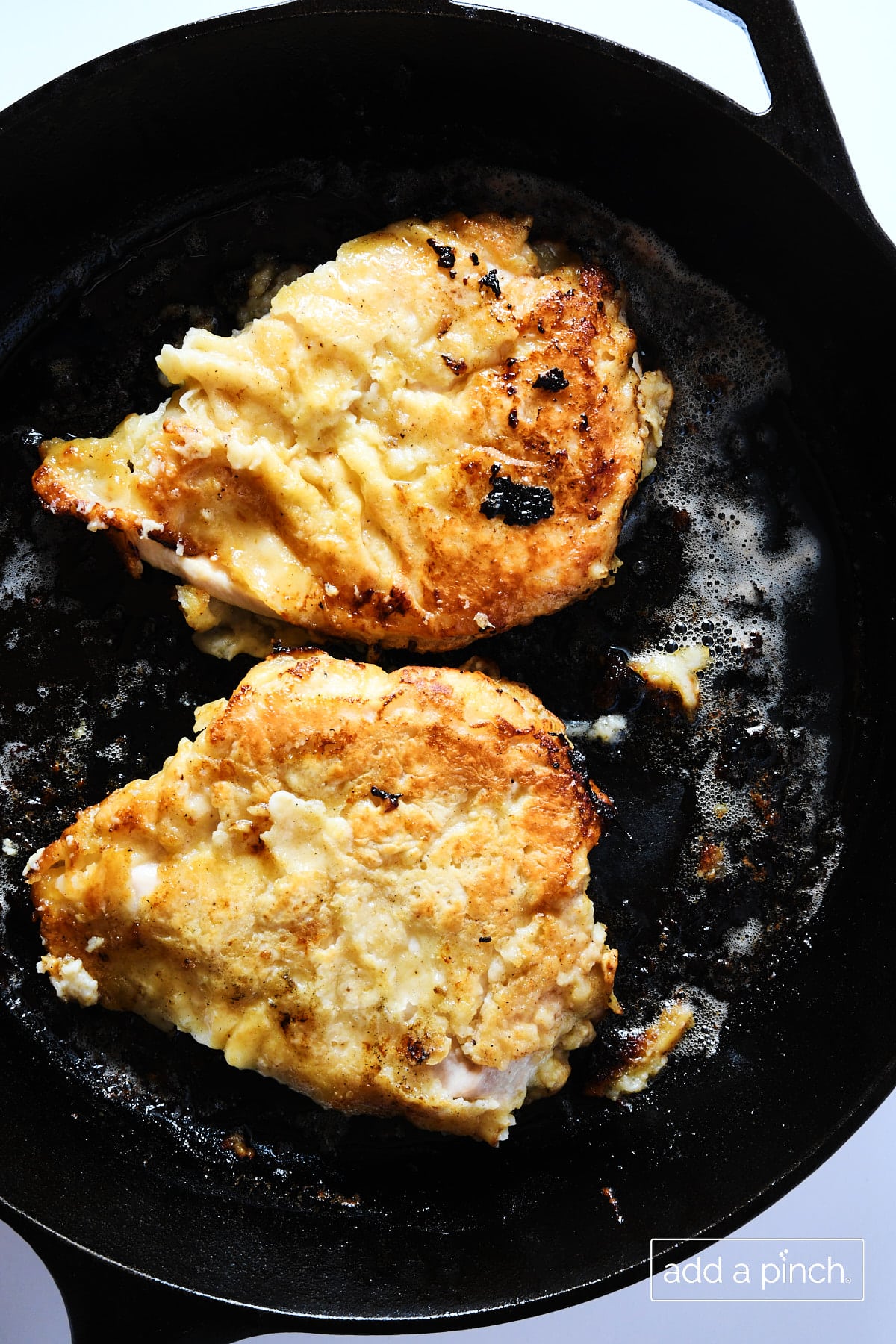 Two oven fried chicken breasts in a cast iron skillet on a white surface.