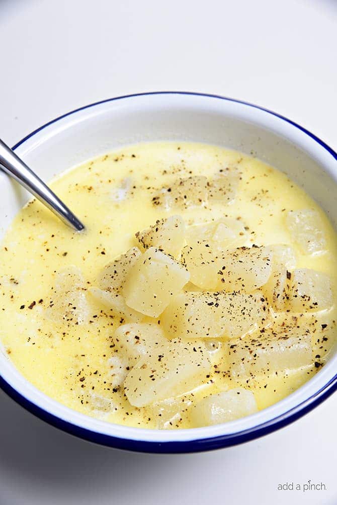 Closeup of spoonful of large chunks of potato in a bowl of Potato Soup seasoned with pepper - addapinch.com