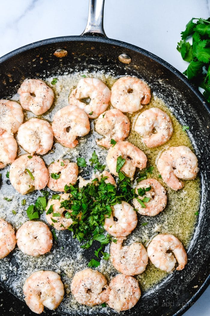 Skillet with melted butter and spices, cooking shrimp and topped with fresh parsley // addapinch.com