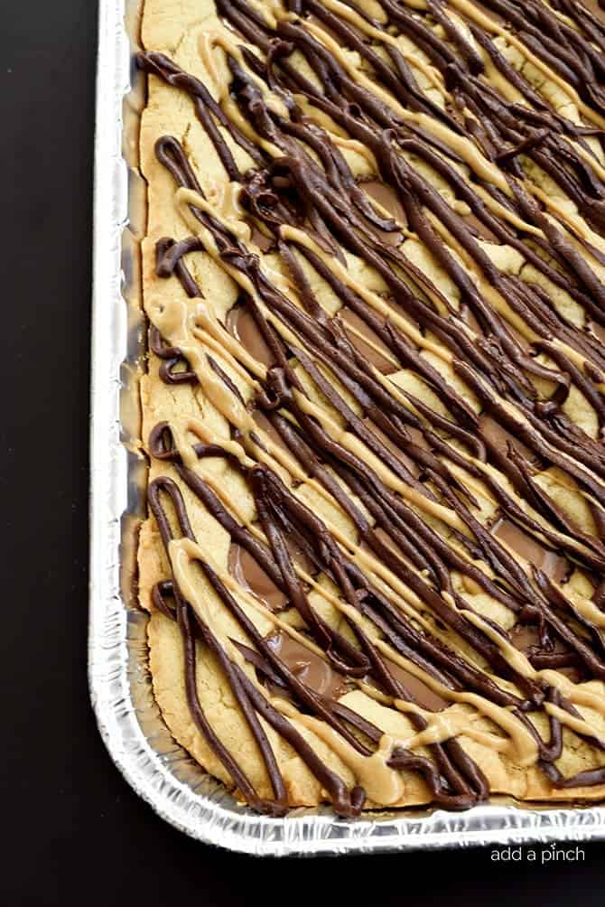 Foil baking pan with peanut butter cup blondies, drizzled with peanut butter and chocolate and full of peanut butter cups // addapinch.com
