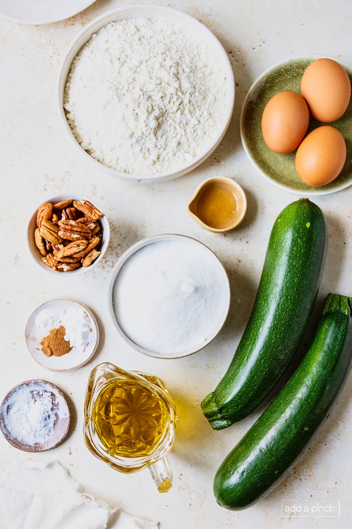 Ingredients used to make homemade zucchini bread on a white surface.