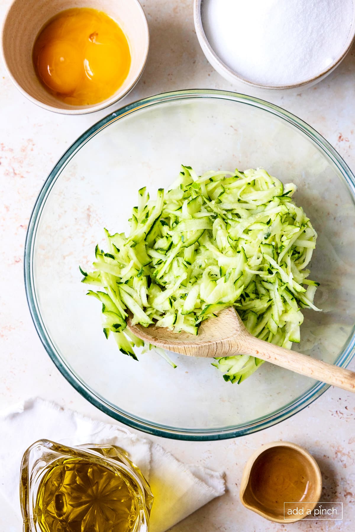 Photo of grated zucchini in a glass bowl with a wooden spoon