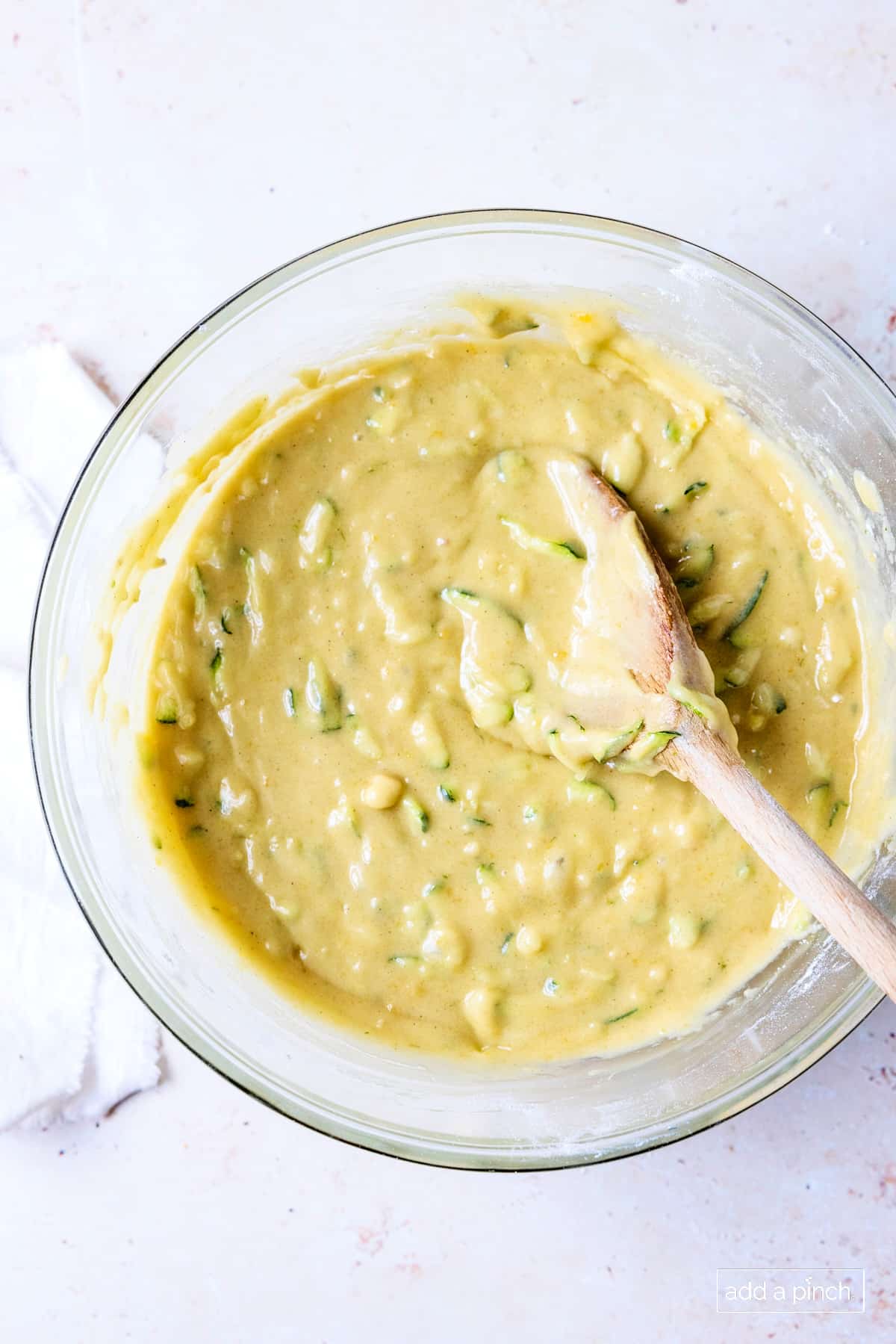 Zucchini bread batter in a glass bowl with a wooden spoon