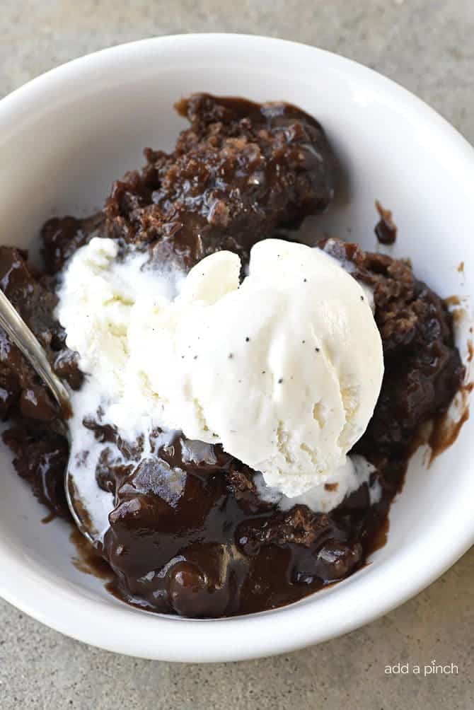 White bowl and spoon with chocolate cobbler topped with vanilla ice cream. 