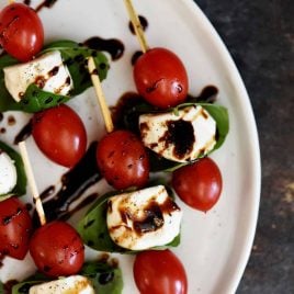 Caprese Salad Skewers of tomatoes, mozzarella, basil, drizzled with balsamic glaze on a white platter.