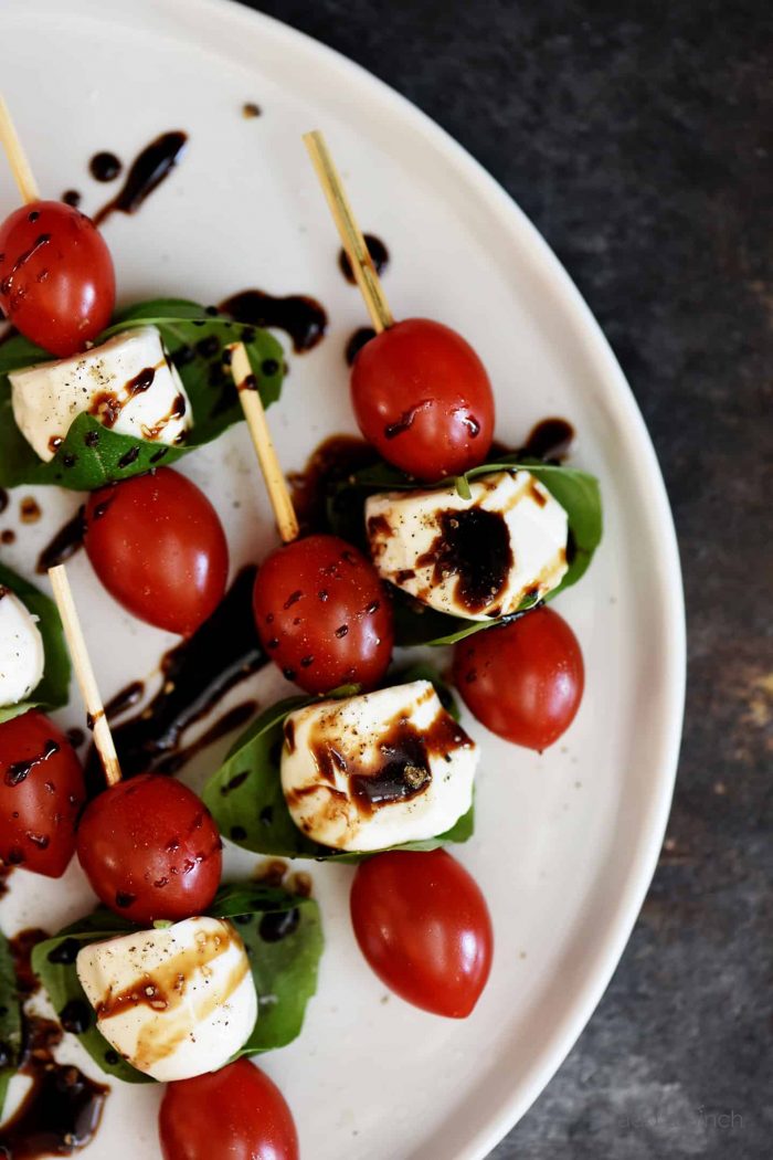 Cherry tomatoes, mozzarella balls, and basil on small wooden skewers are drizzled with balsamic glaze and served on a white platter. // addapinch.com
