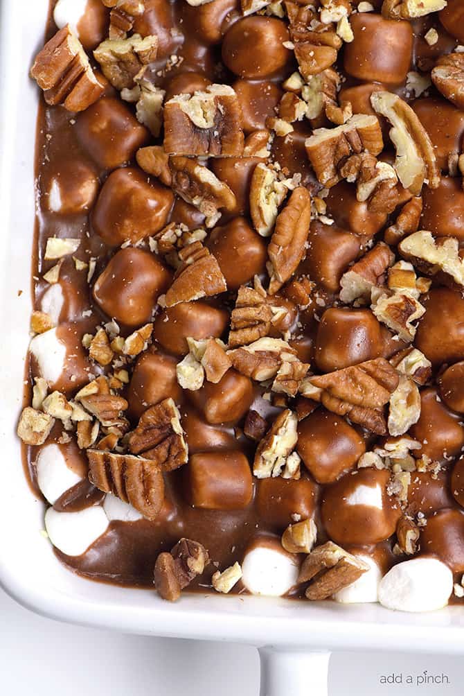 Closeup of white baking dish full of chocolate dessert topped with pecans, marshmallows and chocolate icing // addapinch.com