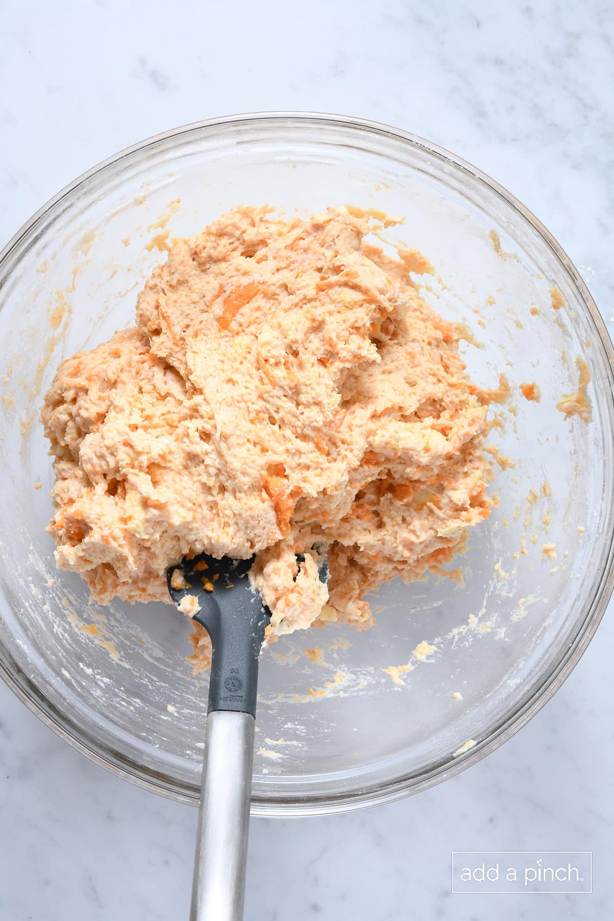 Sweet potato biscuit dough in a glass mixing bowl with a spoon.