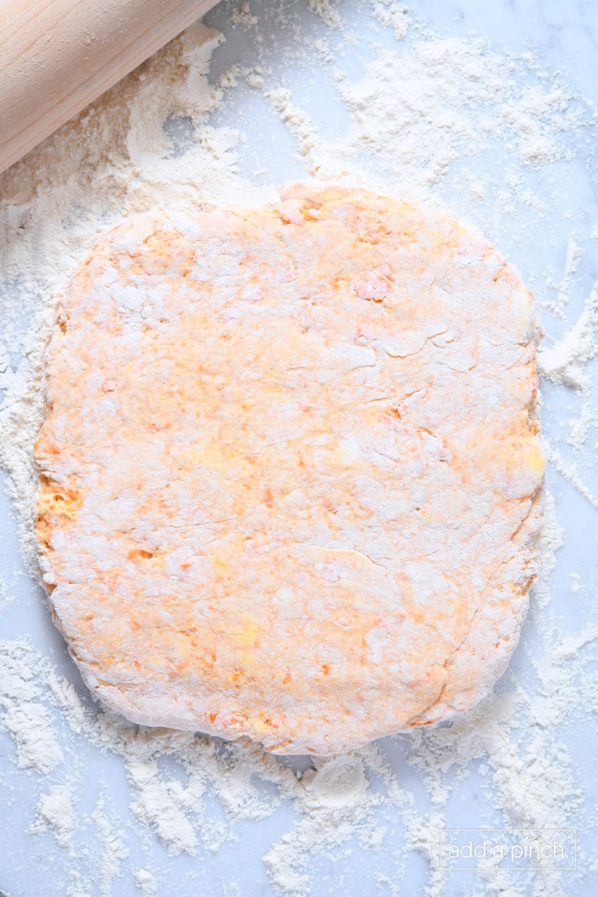 Rolled sweet potato biscuit dough on a floured marble counter with a rolling pin to the edge.