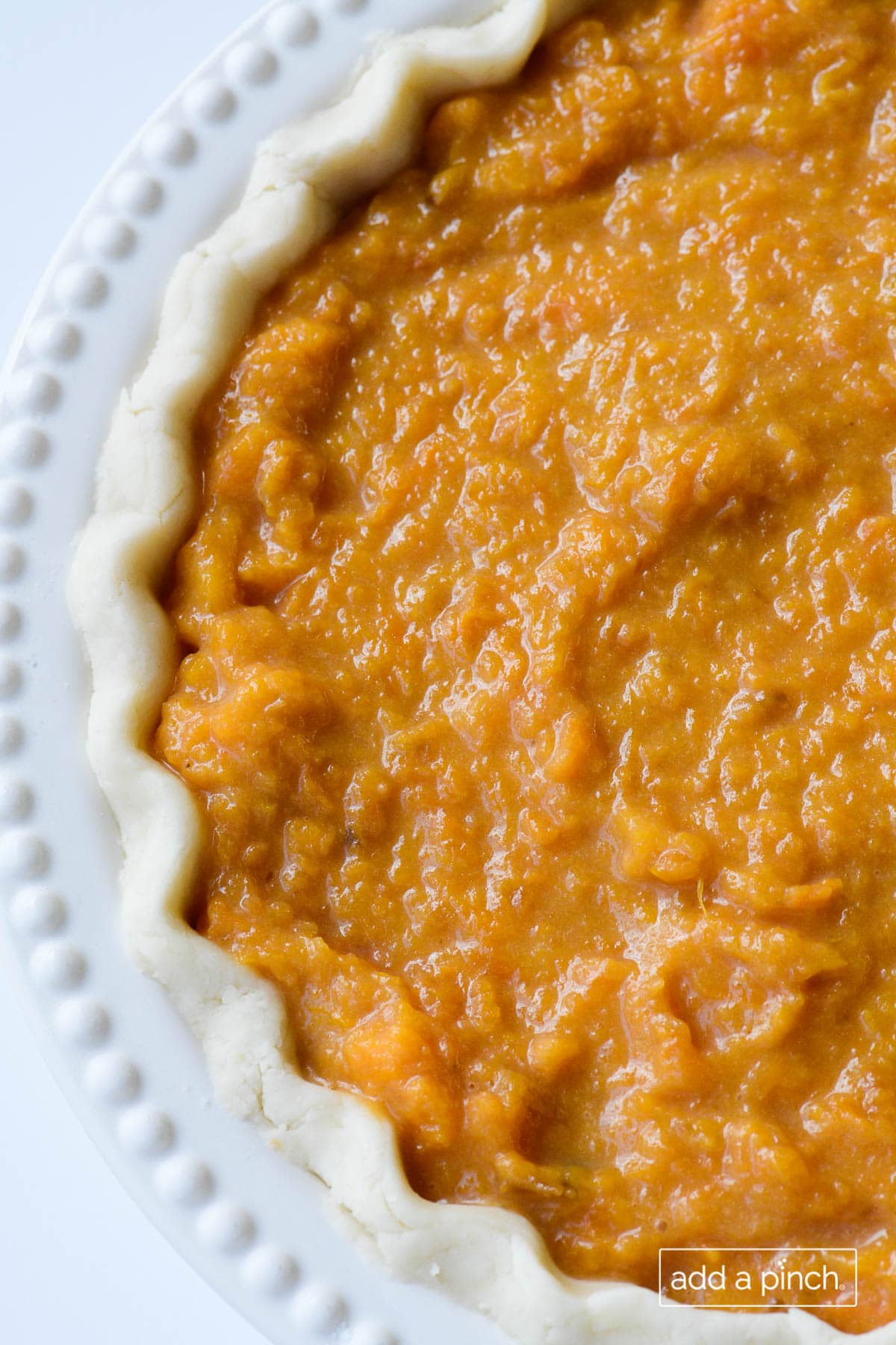Overhead photograph of unbaked sweet potato pie in a white pie plate on white background. 