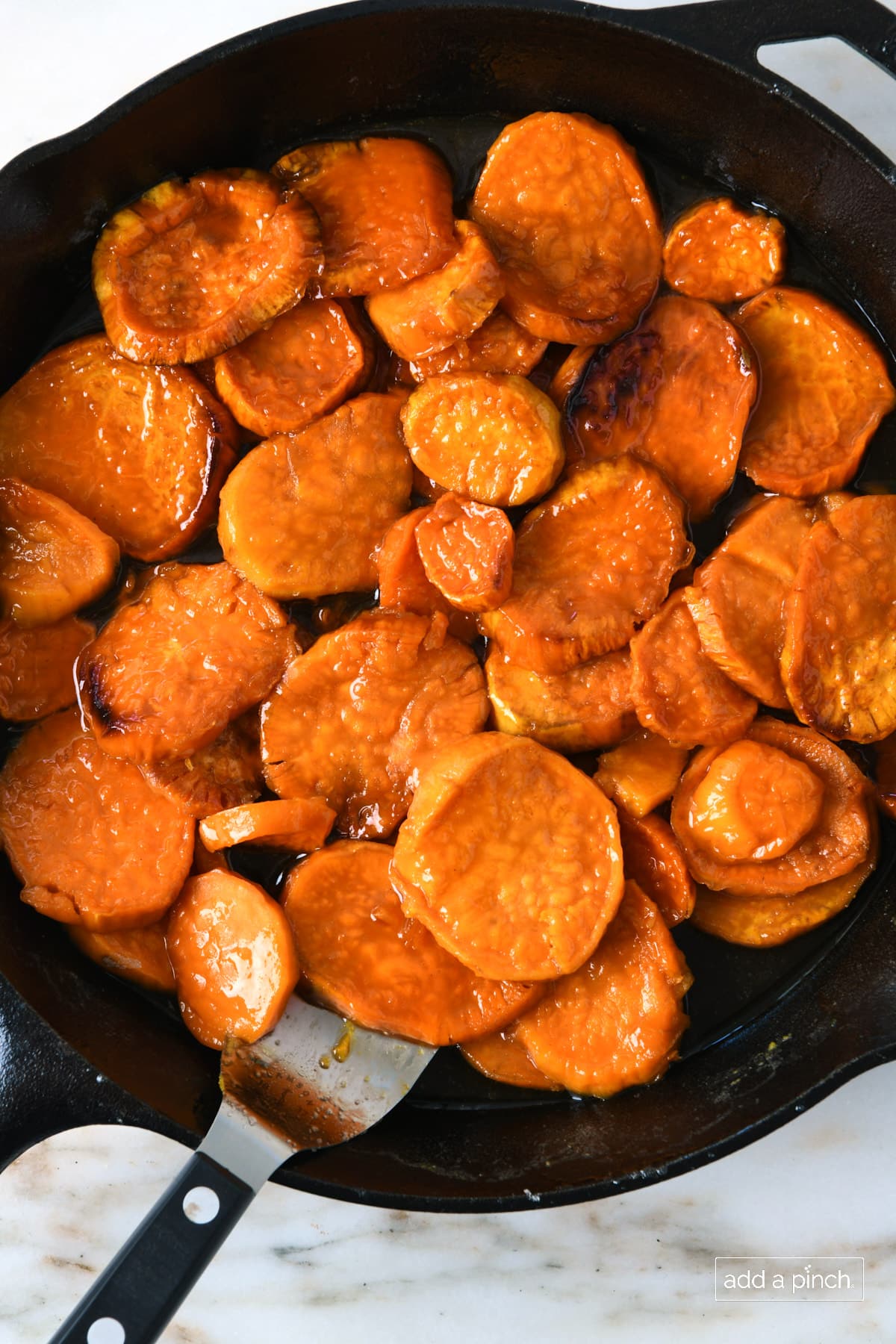 Candied sweet potatoes in a black skillet with a metal server.