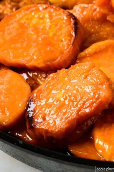 Candied sweet potatoes in a cast iron skillet on a marble countertop.