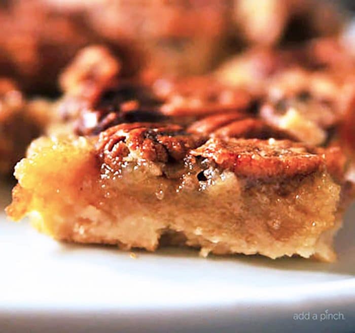 Close up photograph of pecan pie bars on a white cake stand.