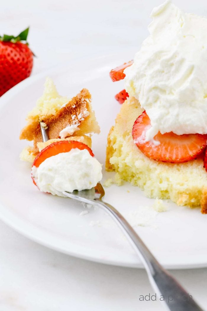 Slice of cream cheese pound cake topped with sliced strawberries and whipped cream with a bite on a fork.