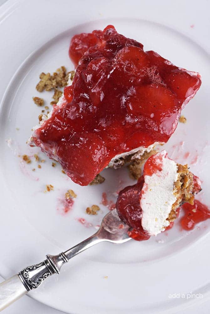 White plate and fork with serving of Strawberry Pretzel Salad showing pretzel crust, creamy layer and strawberry topping. 