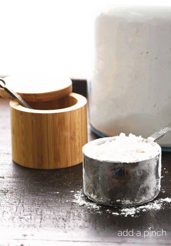 A wooden salt cellar and a measuring cup of flour sits on a stone surface.