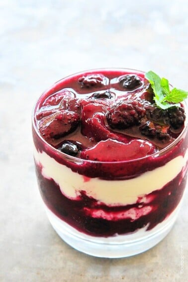 Photo of Triple Berry Parfait in a clear glass topped with a sprig of mint. // addapinch.com