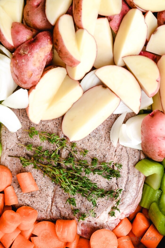 Photograph of potatoes, onion, celery, carrots, thyme surrounding roast to be cooked // addapinch.com