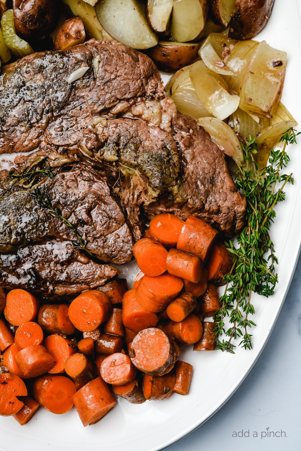 White platter filled with cooked pot roast, carrtos, onions, celery and potatoes with fresh thyme.