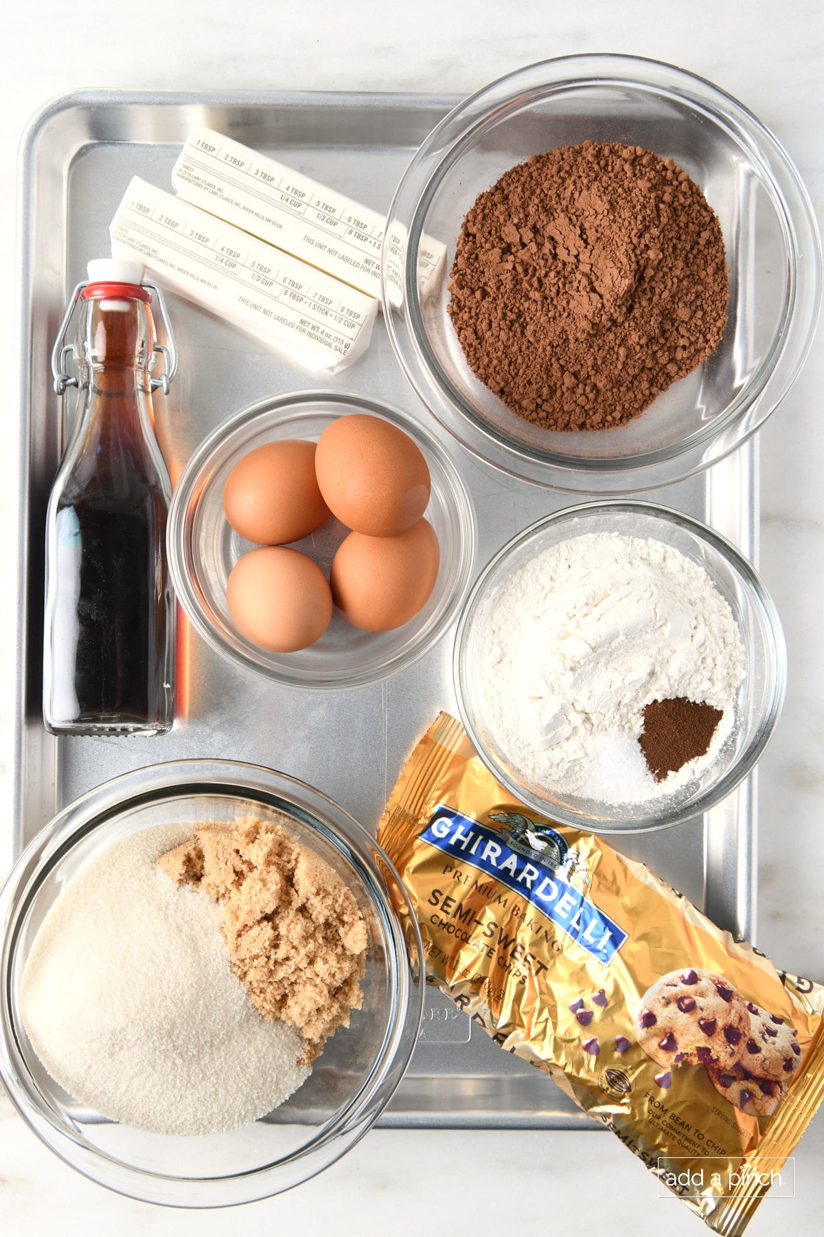 Ingredients to make the best brownies on a metal baking sheet. Butter, cocoa powder, flour, espresso, chocolate chips, brown and granulated sugar, eggs, vanilla extract all on a baking pan. 