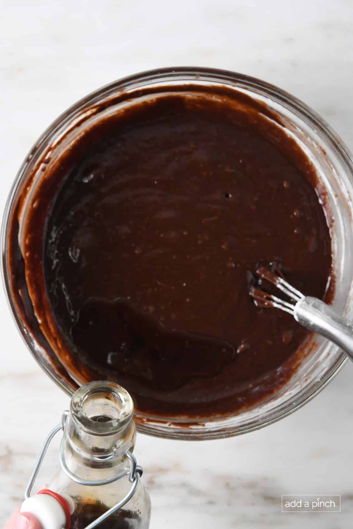 Vanilla extract added to melted brownie batter in a glass bowl with a wire whisk.