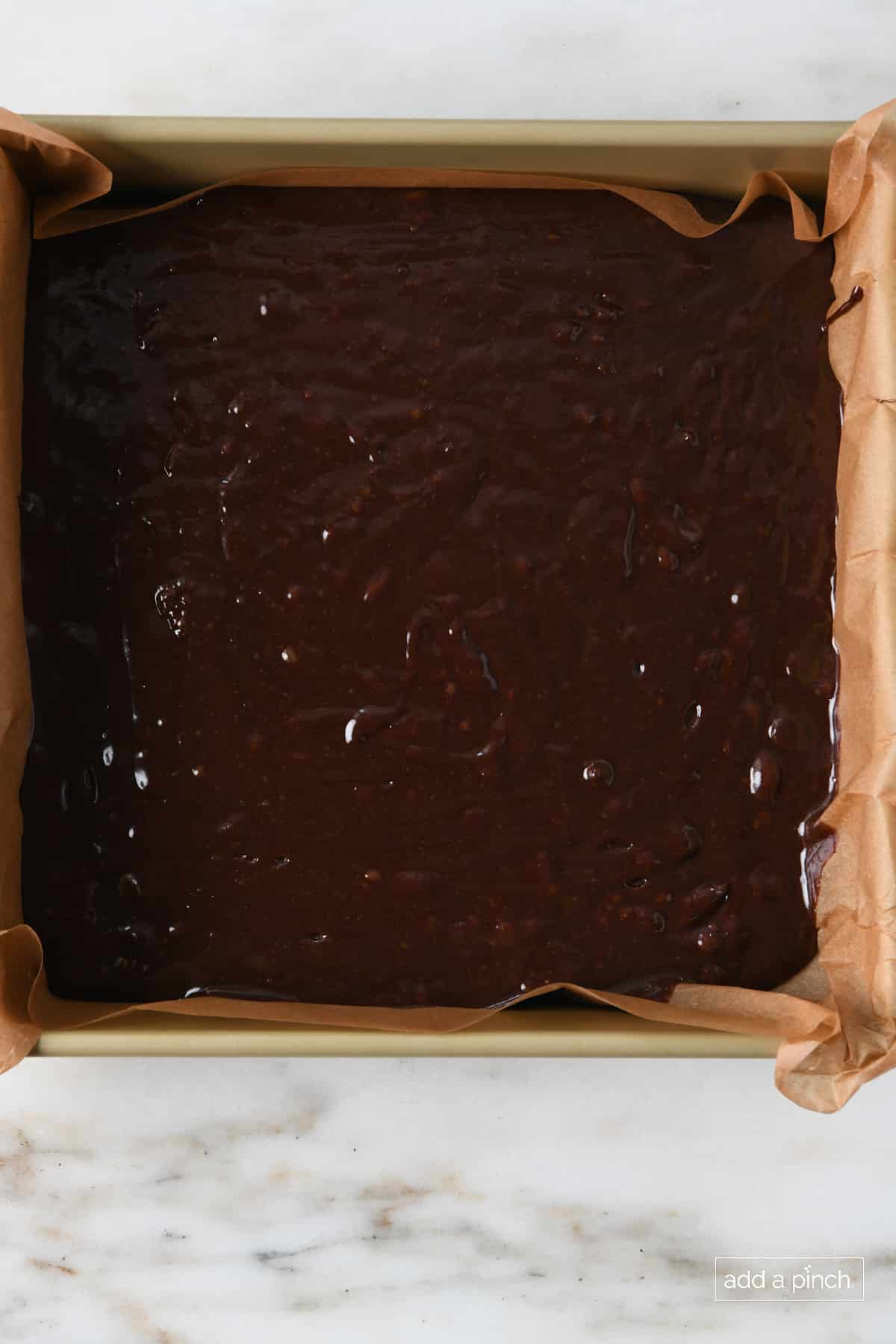 Unbaked chocolate brownie batter spread evenly in a parchment-lined 9x9 baking pan.