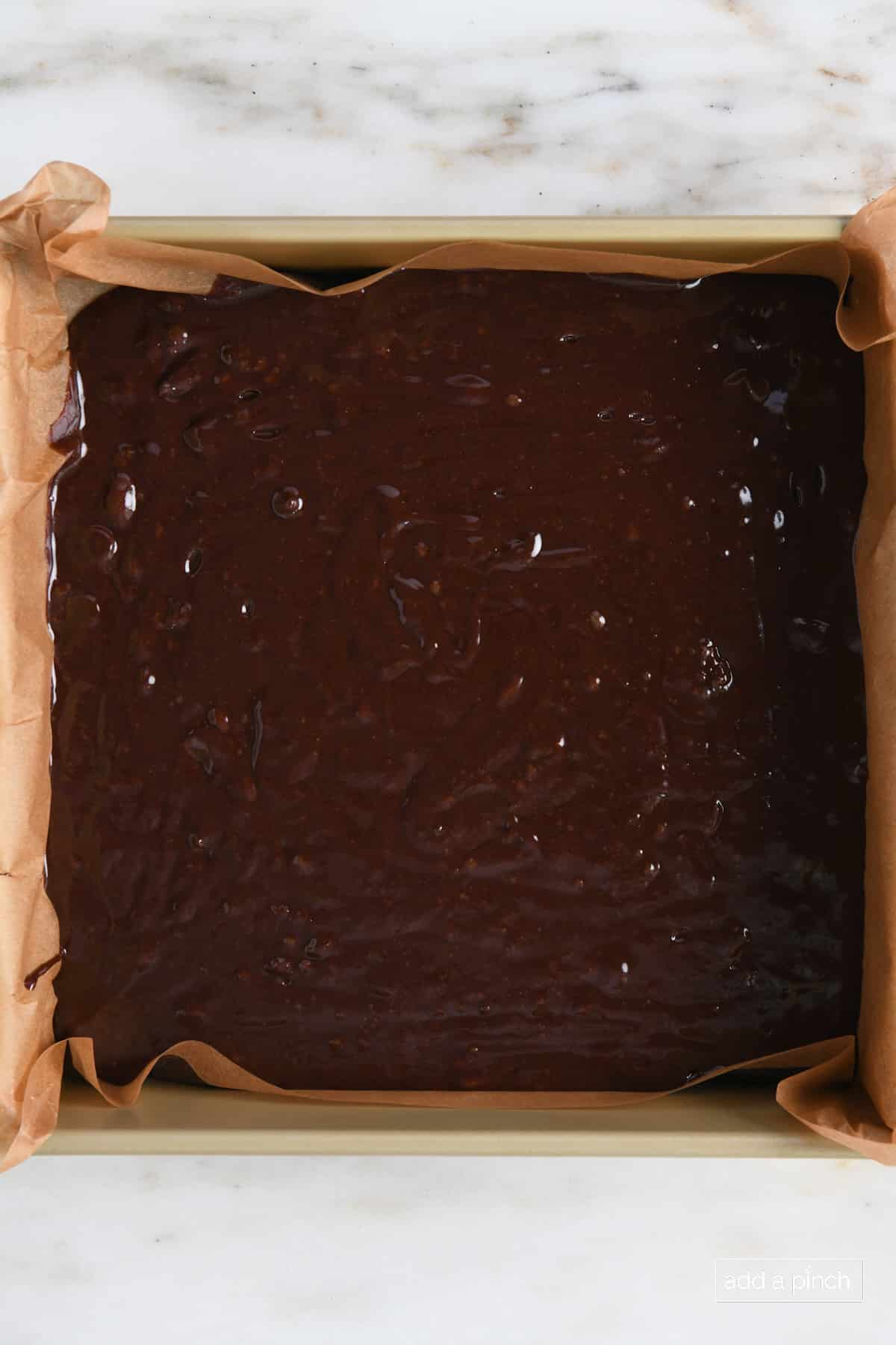 Baking pan lined with parchment filled with chocolate brownie batter. 